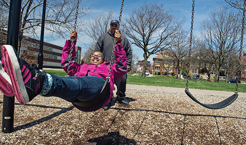 Child is pushed on a swing, smiling on a sunny day
