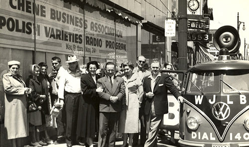 Old photo of a group of people outside of the Chene Business Association/Polish Varieties Radio Program, next to a Volkswagen bus