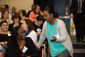 Two women wearing name tags converse in a crowd of people.