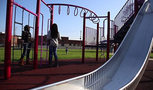 Two girls stand on a playground next to monkey bars.