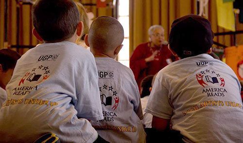 Children wearing matching t-shirts sit in the Ginsberg Center listening to a woman speak.