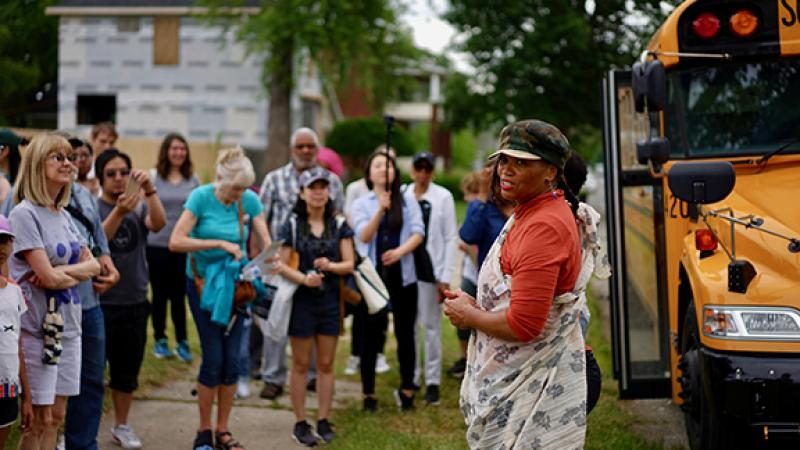 Diane Hoy stands amongst a crowd of people and a school bus, looking back toward the camera.